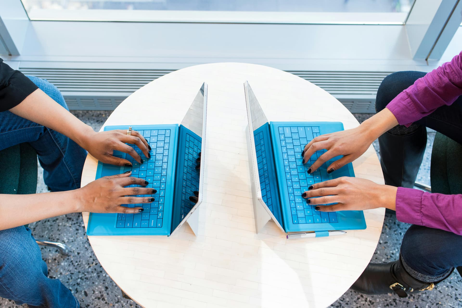 Two people sitting infront of each other working on their laptops.