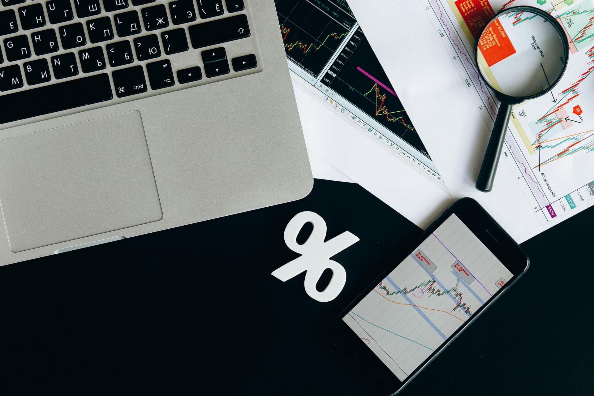 Laptop, phone, and documents on desk with a percentage symbol.