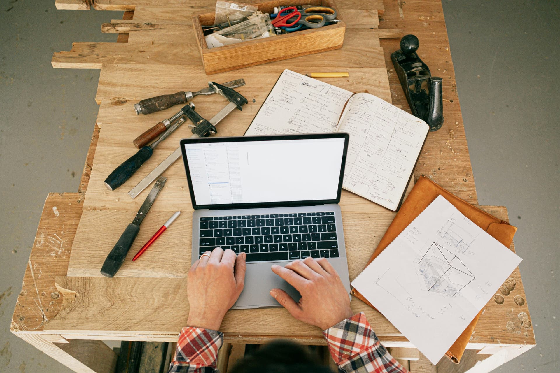 A worker using a laptop with other tools on the desk.