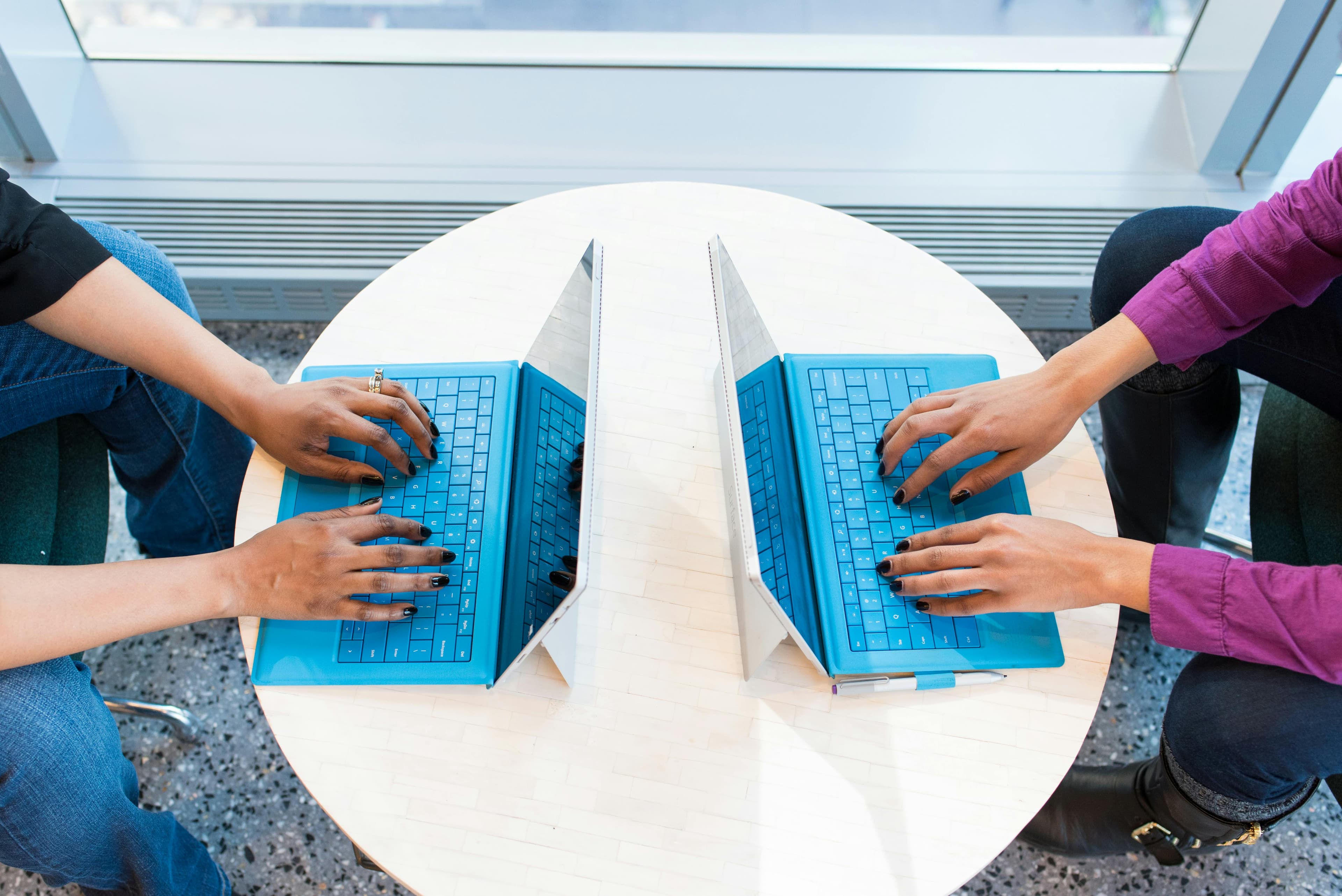 Two people sitting infront of each other working on their laptops.